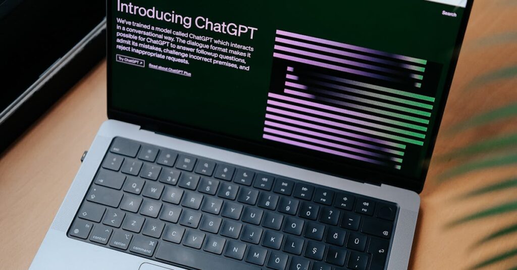 A sleek laptop on a wooden desk showing the ChatGPT homepage by a window.